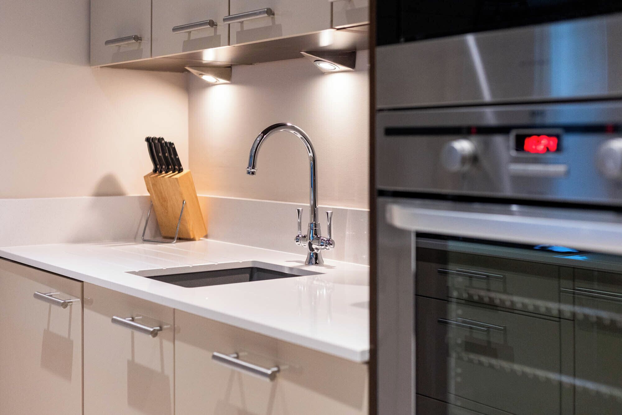 A modern kitchen with a stainless steel oven, a sink with a faucet, and a knife block.