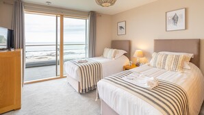 A hotel room with two beds, a TV, a balcony with a view of the sea, and a ceiling light fixture. - The Sands - Sea Front Apartments (Scarborough)