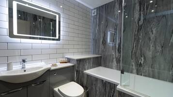 Un baño moderno con salpicadero de mármol, un lavabo blanco, un inodoro y una cabina de ducha con paredes de cristal.
