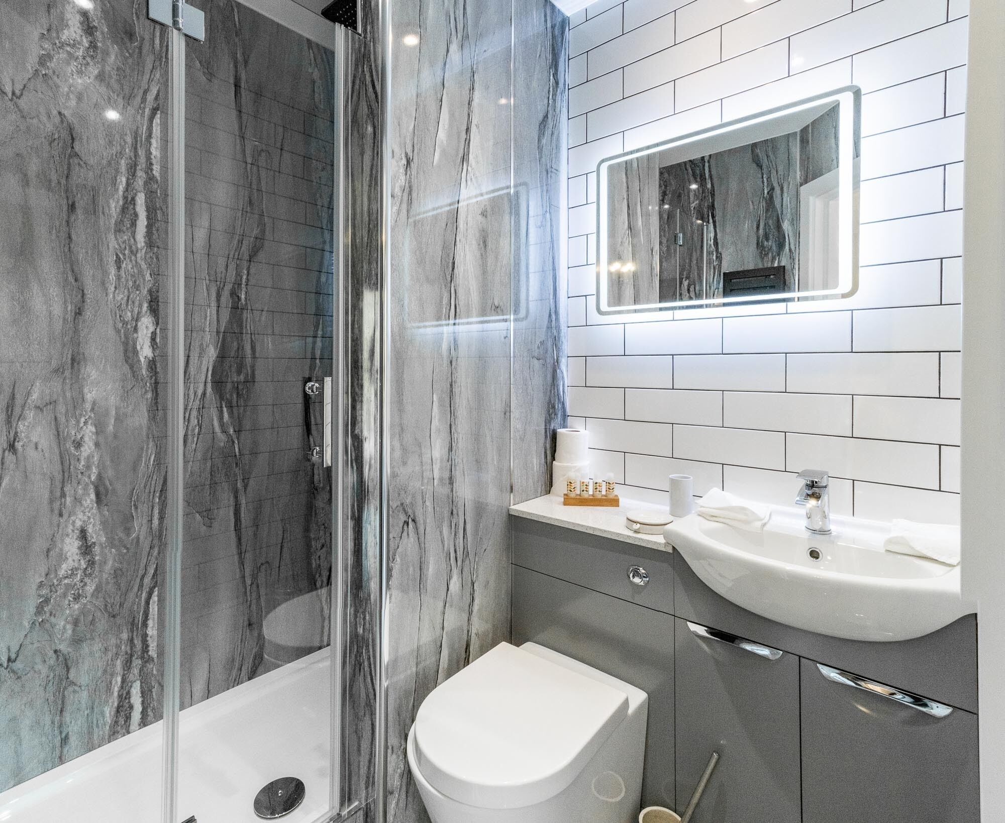 Un baño moderno con ducha de vidrio, inodoro blanco y lavabo con espejo.