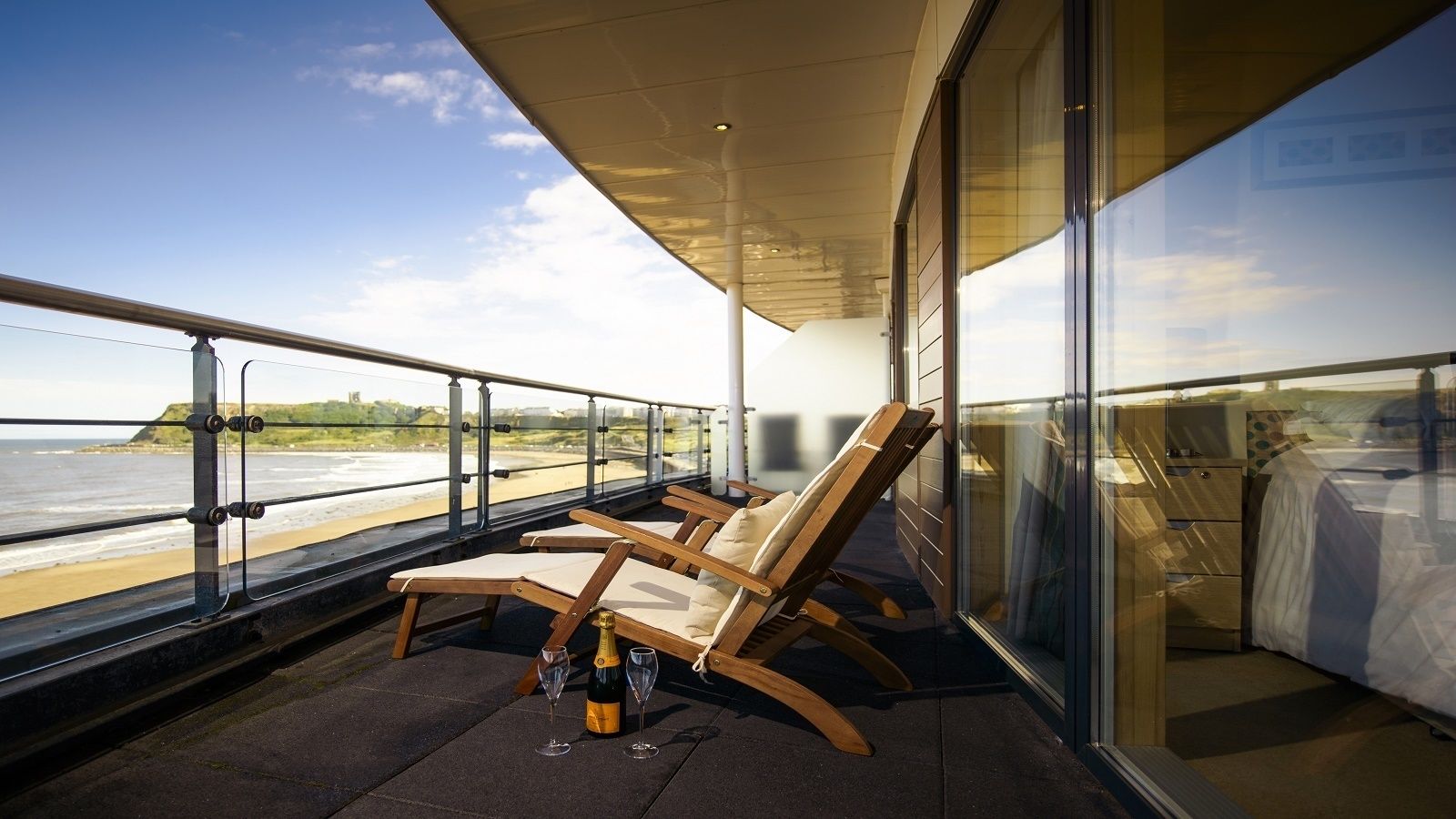 Un balcon avec deux fauteuils de jardin en bois, une bouteille de champagne et deux verres.