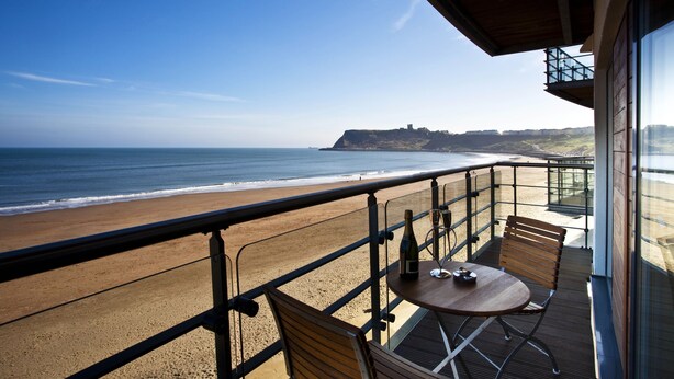 A balcony with a view of the beach and ocean, featuring a table with chairs and a bottle. - The Sands - Sea Front Apartments (Scarborough)