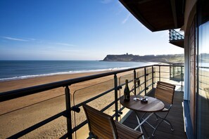 Un balcón con vistas a la playa y el océano, que incluye una mesa con sillas y una botella.