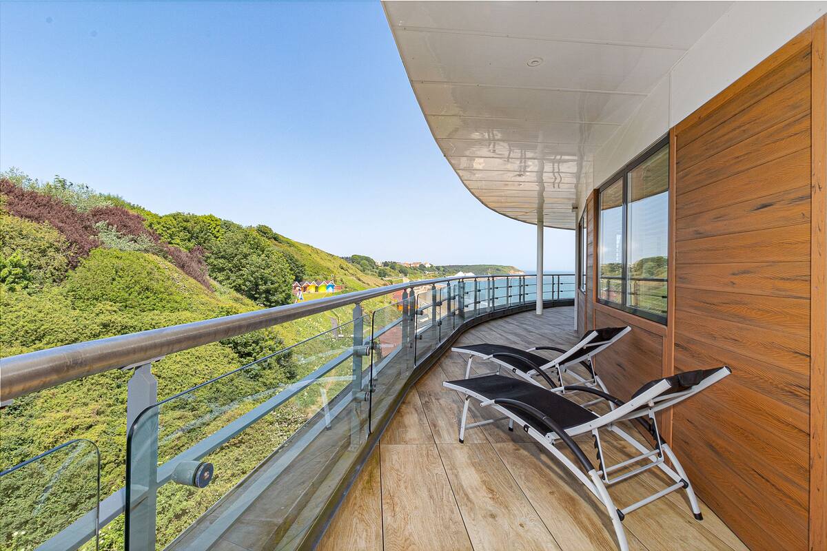 A balcony with a wooden floor, metal railing, and two reclining chairs.