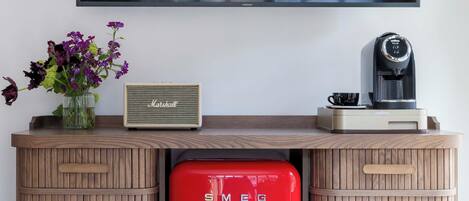 Una sala de estar moderna con un refrigerador rojo, una cafetera y un televisor de pantalla plana montado en la pared.