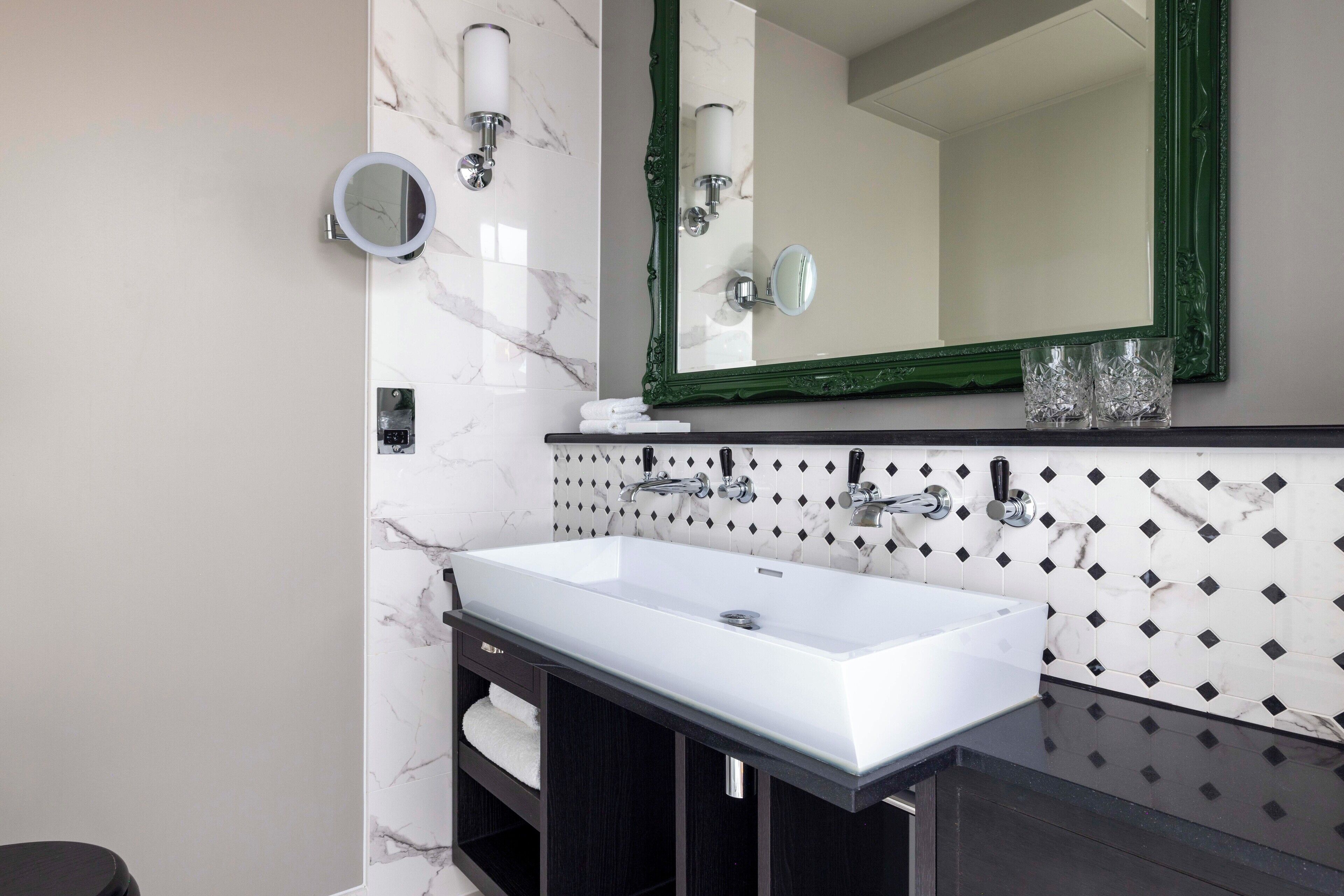 Une salle de bain moderne avec un grand lavabo blanc, des meubles en bois foncé et un miroir à cadre vert.