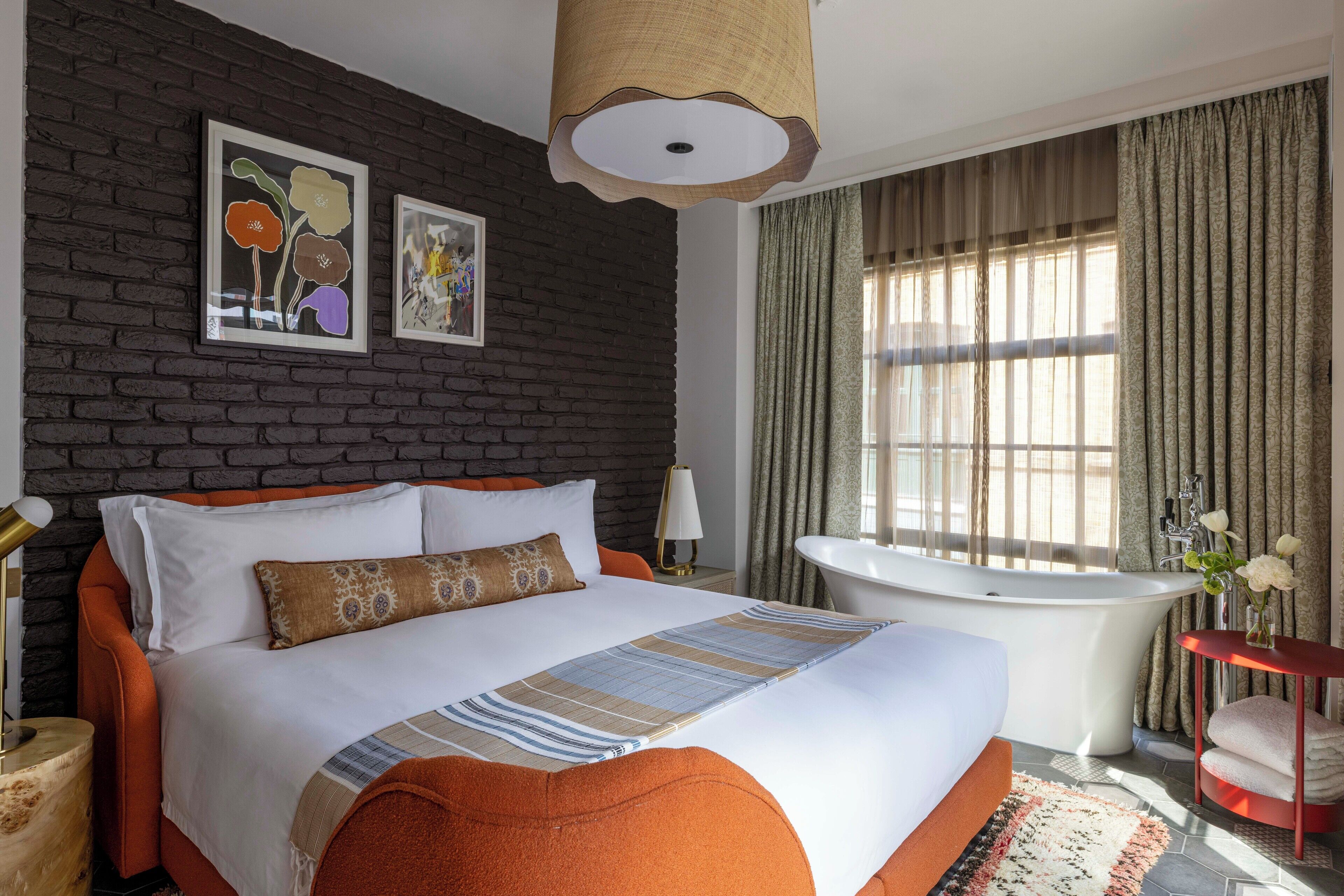 A modern bedroom with a brick wall, a large bed, a bathtub, and a window with curtains.
