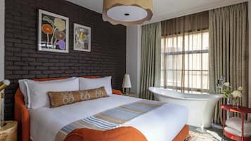 A modern bedroom with a brick wall, a large bed, a bathtub, and a window with curtains.