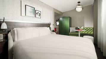 A hotel room with a large bed, a green sofa, a small table with a vase, and a green wardrobe.