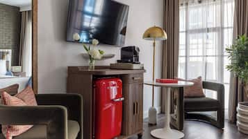 A modern hotel room with a flat-screen TV, a red refrigerator, a coffee maker, a small table, and a comfortable seating area.