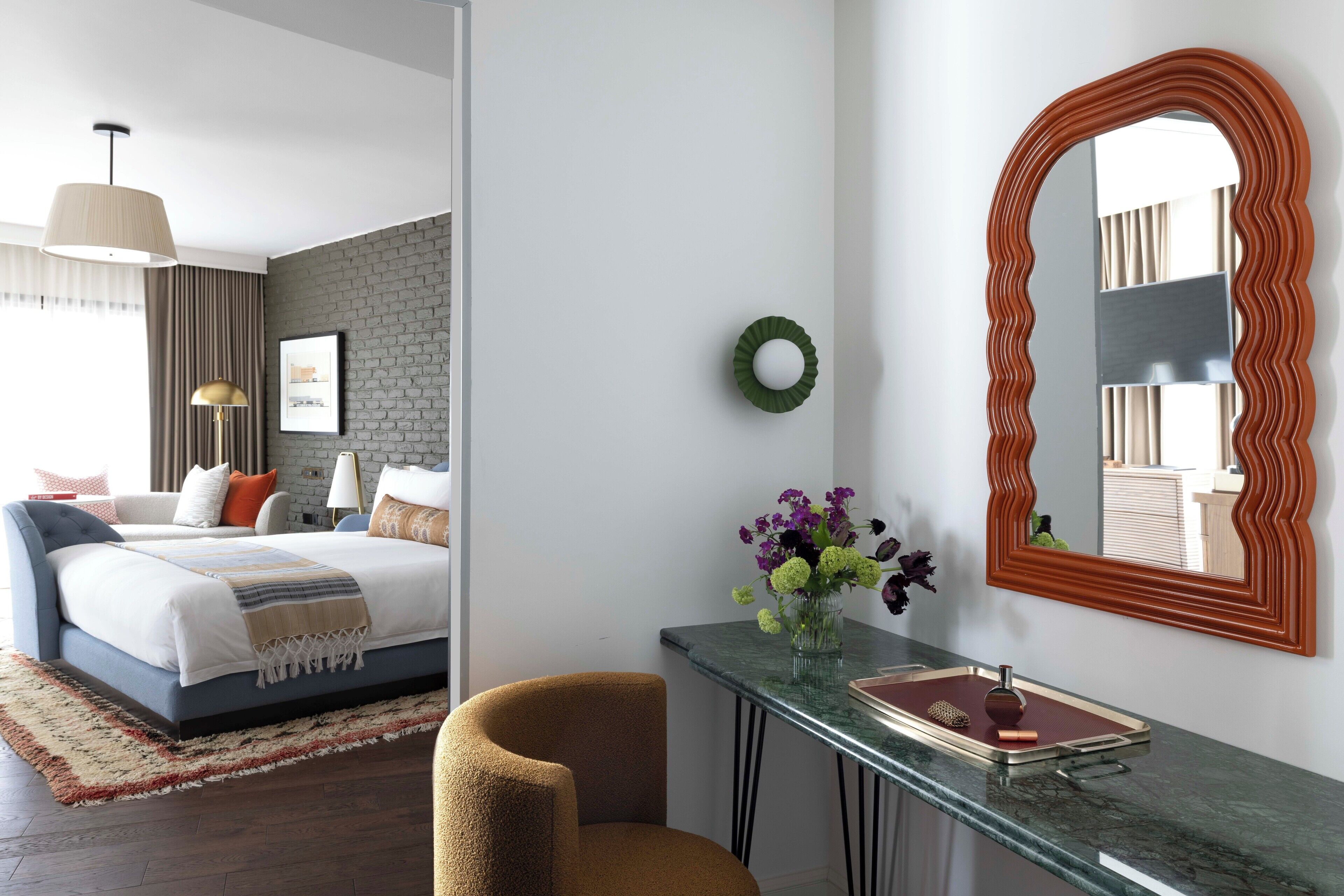 Une chambre d’hôtel moderne, équipée d’un lit, d’un bureau avec un miroir, d’un vase avec des fleurs et offrant une vue sur la ville.