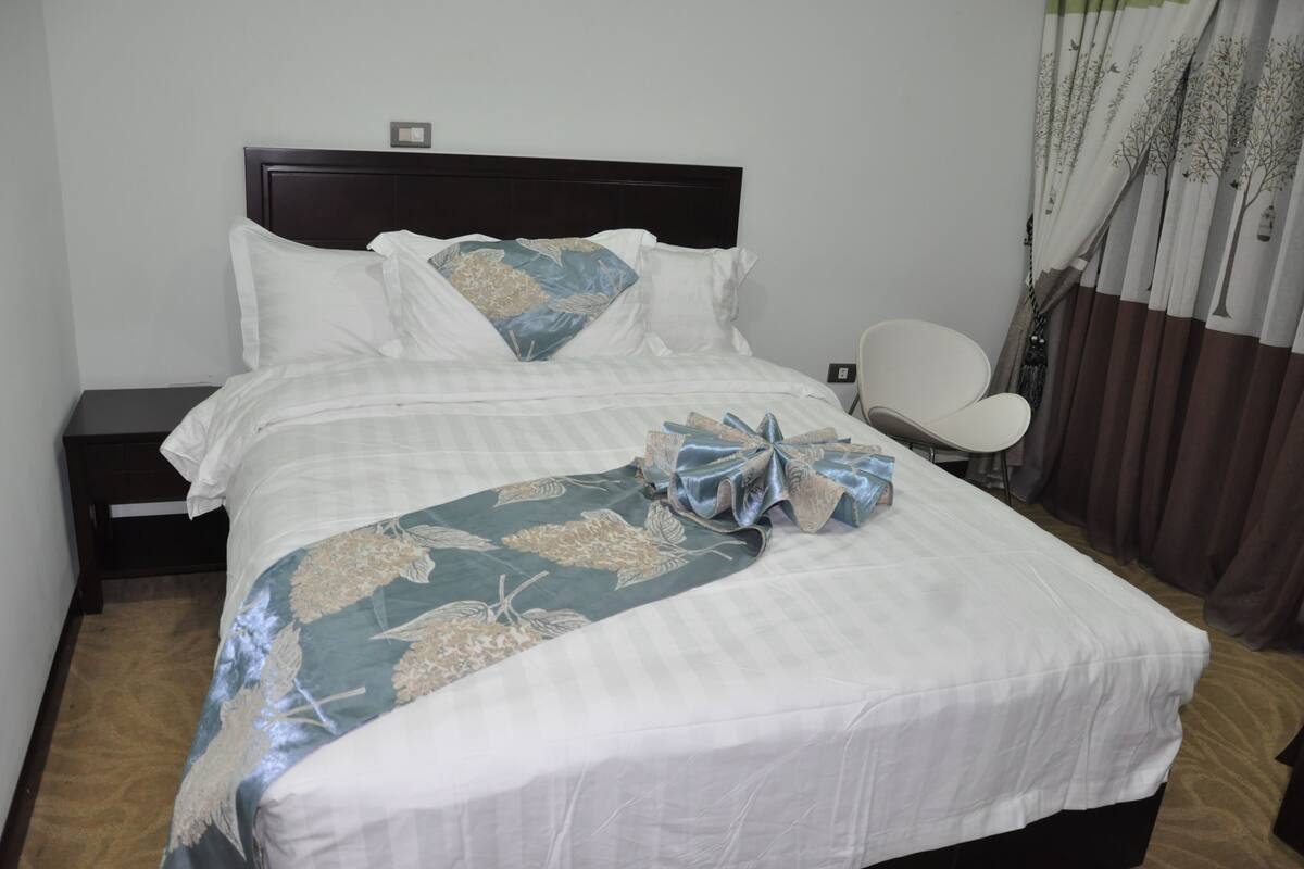 A neatly made bed with a floral bedspread, a bedside table, and a chair.