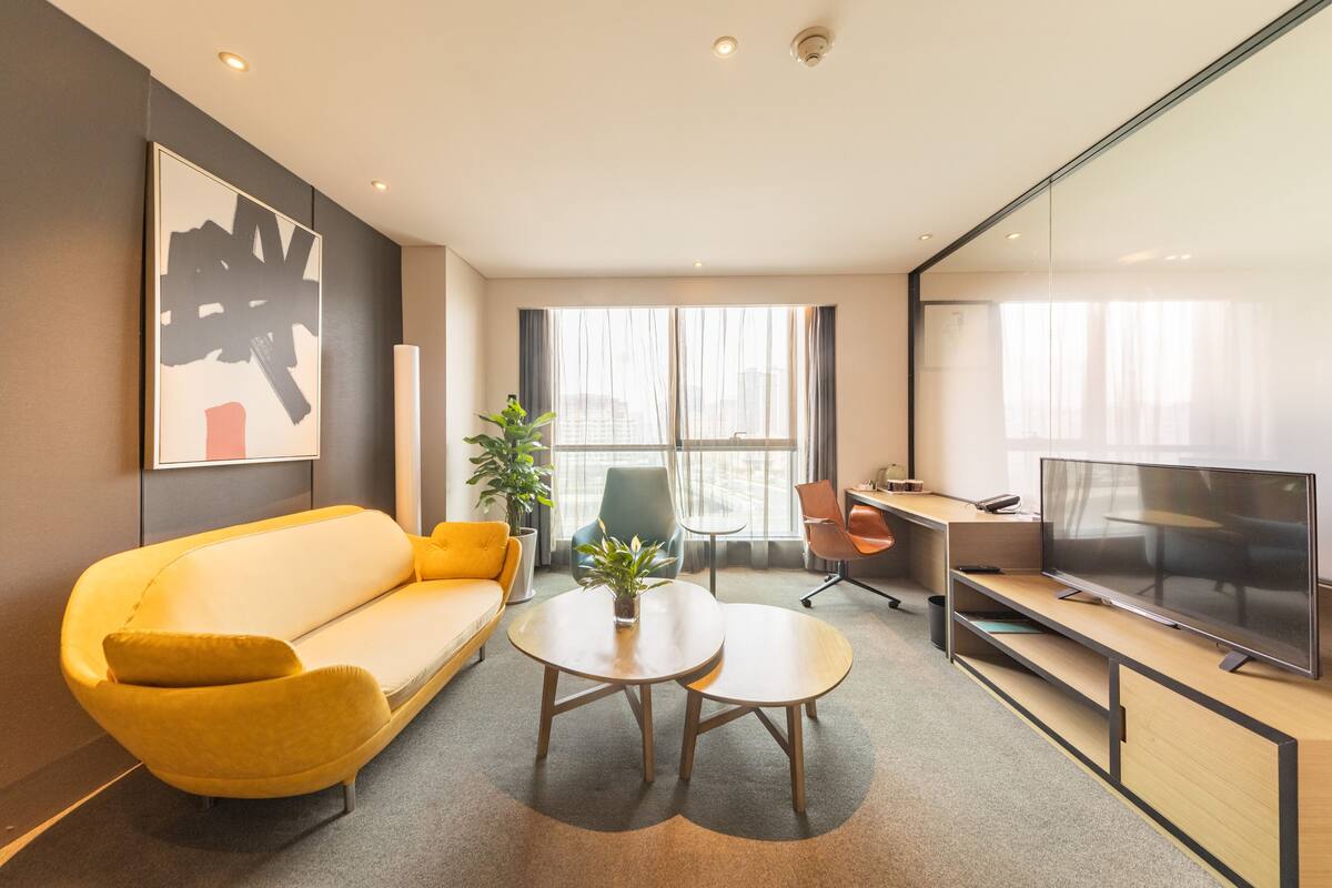 A modern living room with a yellow sofa, a coffee table, a TV, and a desk with a computer.