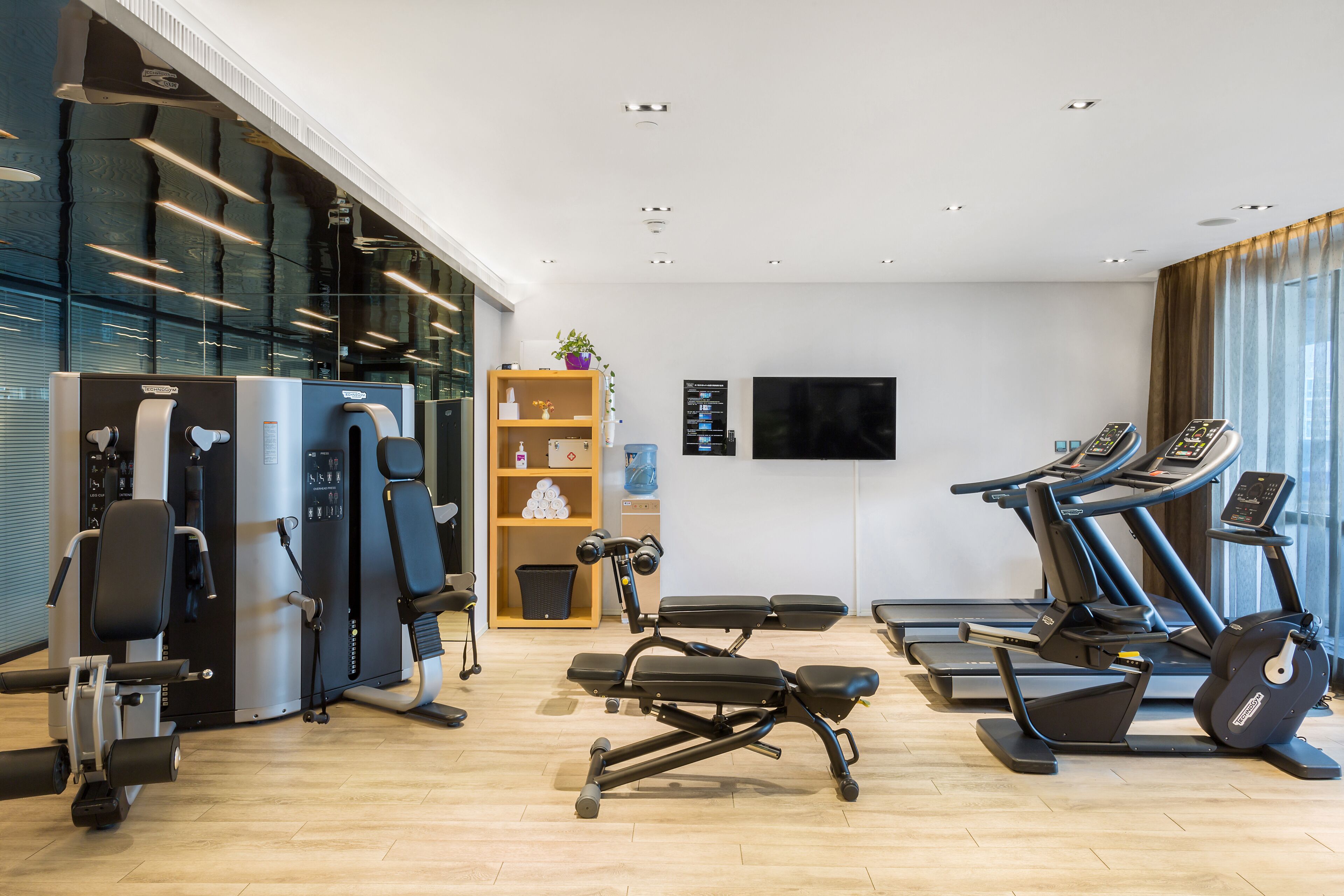 Une salle de sport moderne équipée de machines de cardio, d’appareils de musculation et dotée d’une grande fenêtre laissant entrer la lumière naturelle.