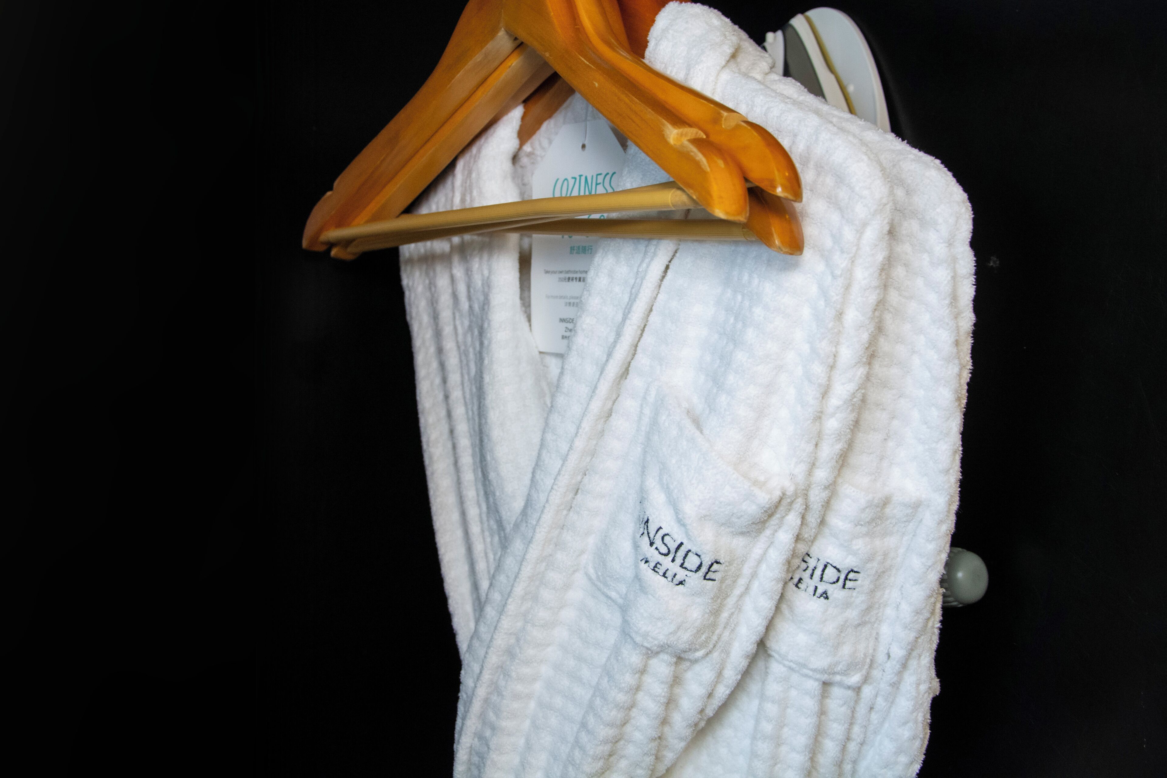 A white robe with "INSIDE" and "SIDE" text, hanging on a wooden hanger against a dark background.