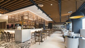 A modern bar area with a central counter, multiple seating options, and a patterned floor. - INNSiDE by Meliá Zhengzhou (Zhengzhou)