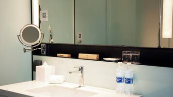 Un baño de hotel con lavamanos, espejo y dos botellas de agua.