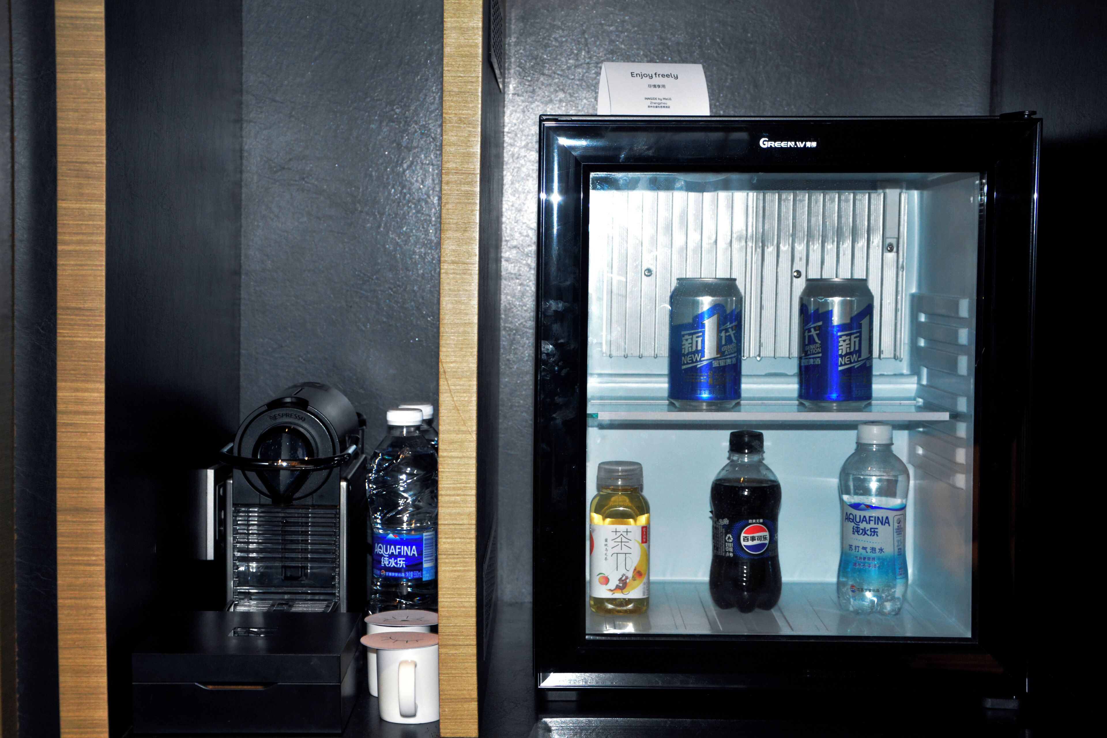 A minibar with a refrigerator containing beverages, a coffee machine, and a water dispenser.