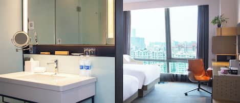 Una camera d'albergo con un'ampia finestra, un letto, una scrivania e un bagno con lavandino e specchio.