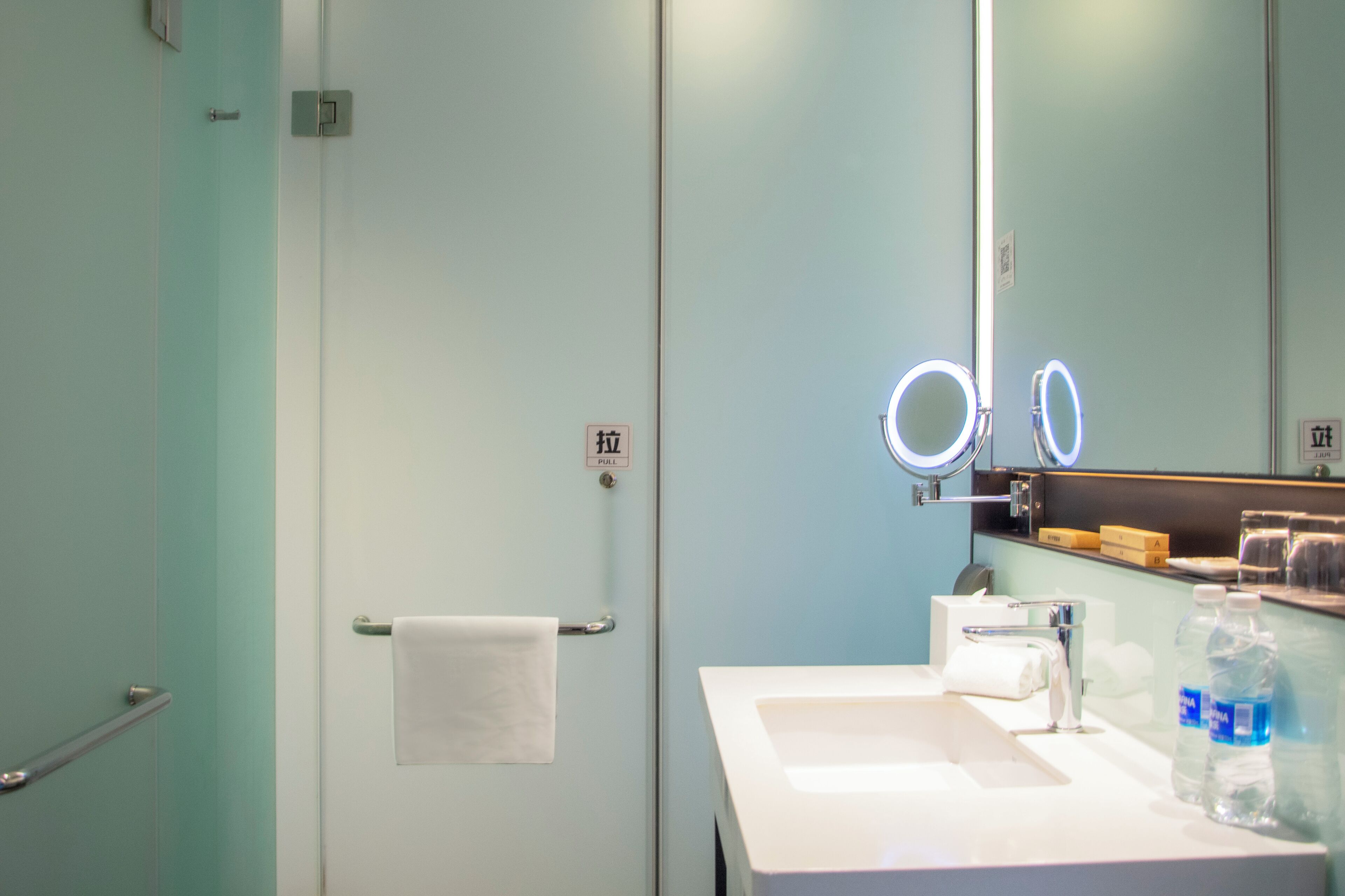 Un baño con un lavabo blanco, un espejo con iluminación, un perchero y una puerta con picaporte.