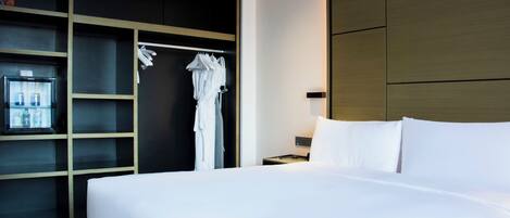 A hotel room with a large bed, a wardrobe with shelves, and a small table with a lamp.