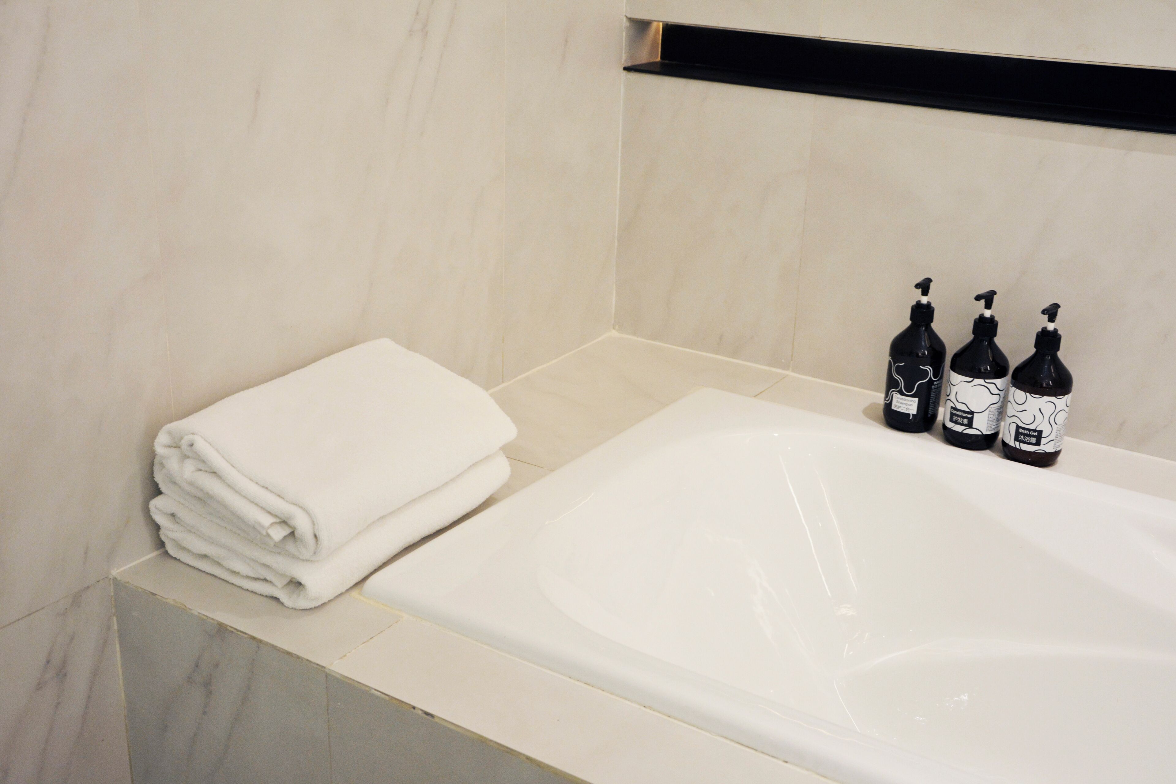 Een badkamer met een witte badkuip, een stapel witte handdoeken en drie zwarte flessen met verstuivers.