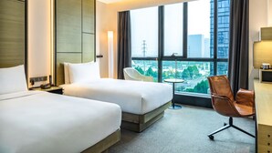 A hotel room with two beds, a desk, a chair, and a large window offering a city view. - INNSiDE by Meliá Zhengzhou (Zhengzhou)