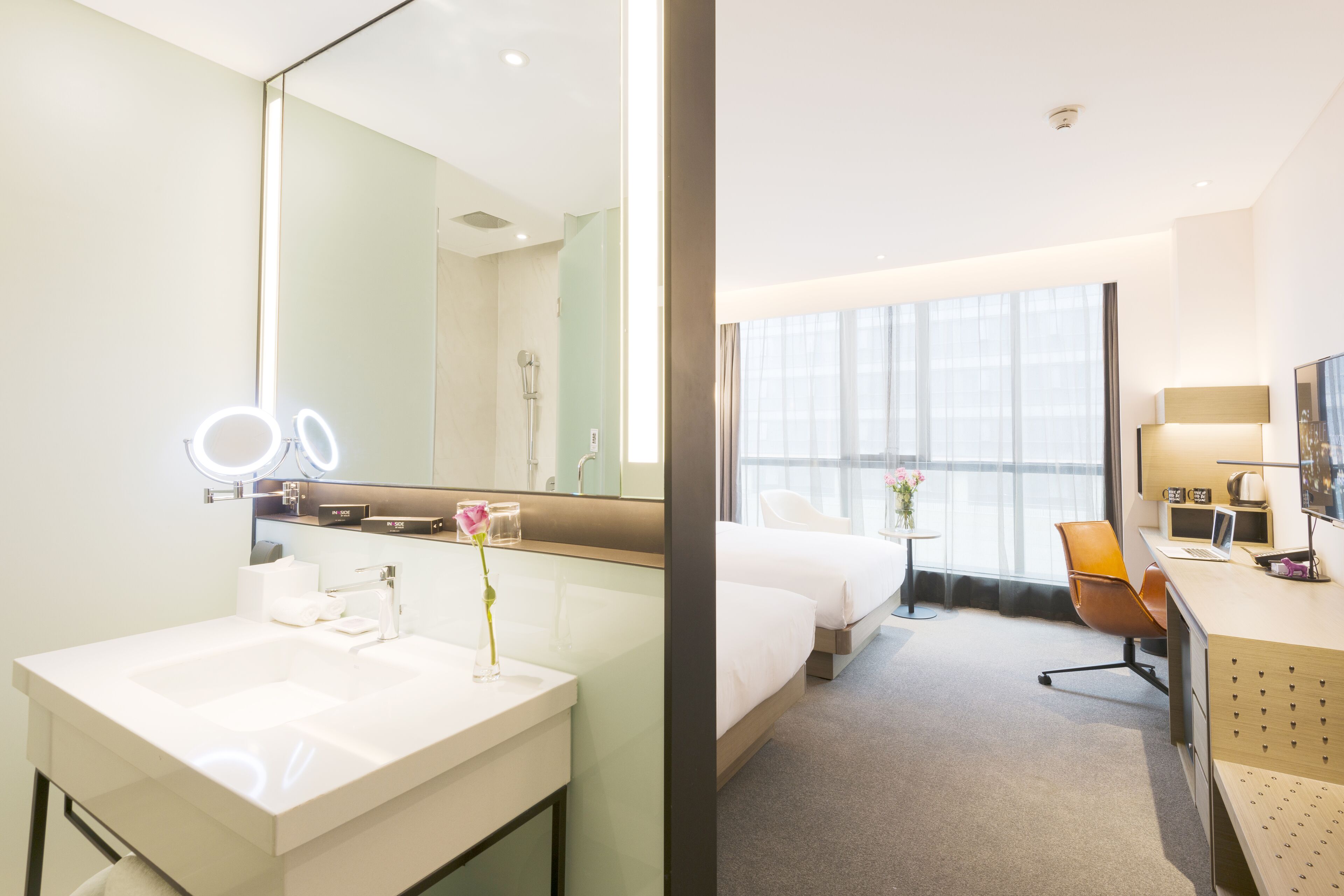 Une chambre d’hôtel avec un grand miroir, un lavabo, une douche, un lit, un bureau avec une chaise et une télévision.