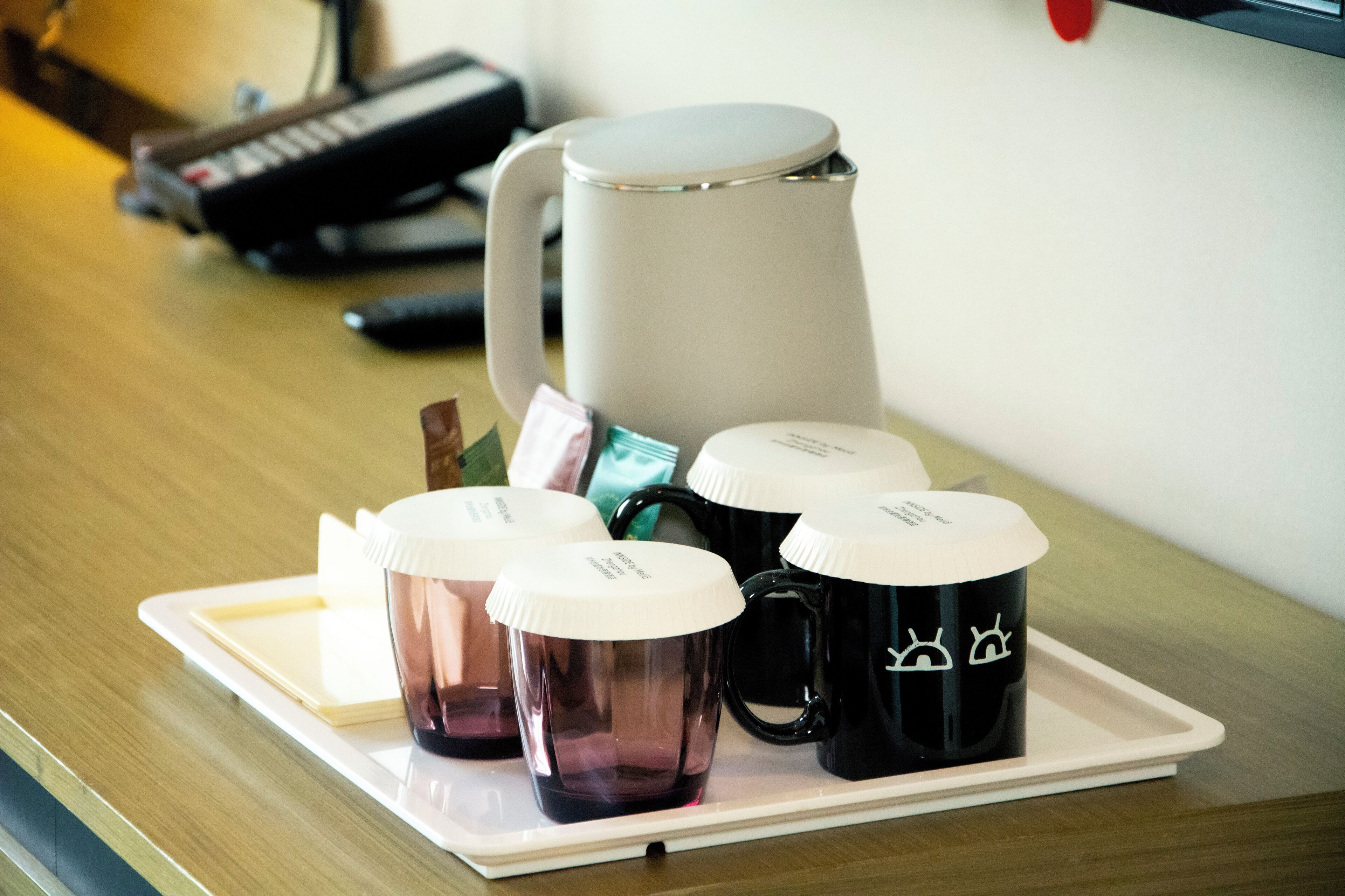 A tray with a coffee maker, several mugs, and a notebook on a wooden table.