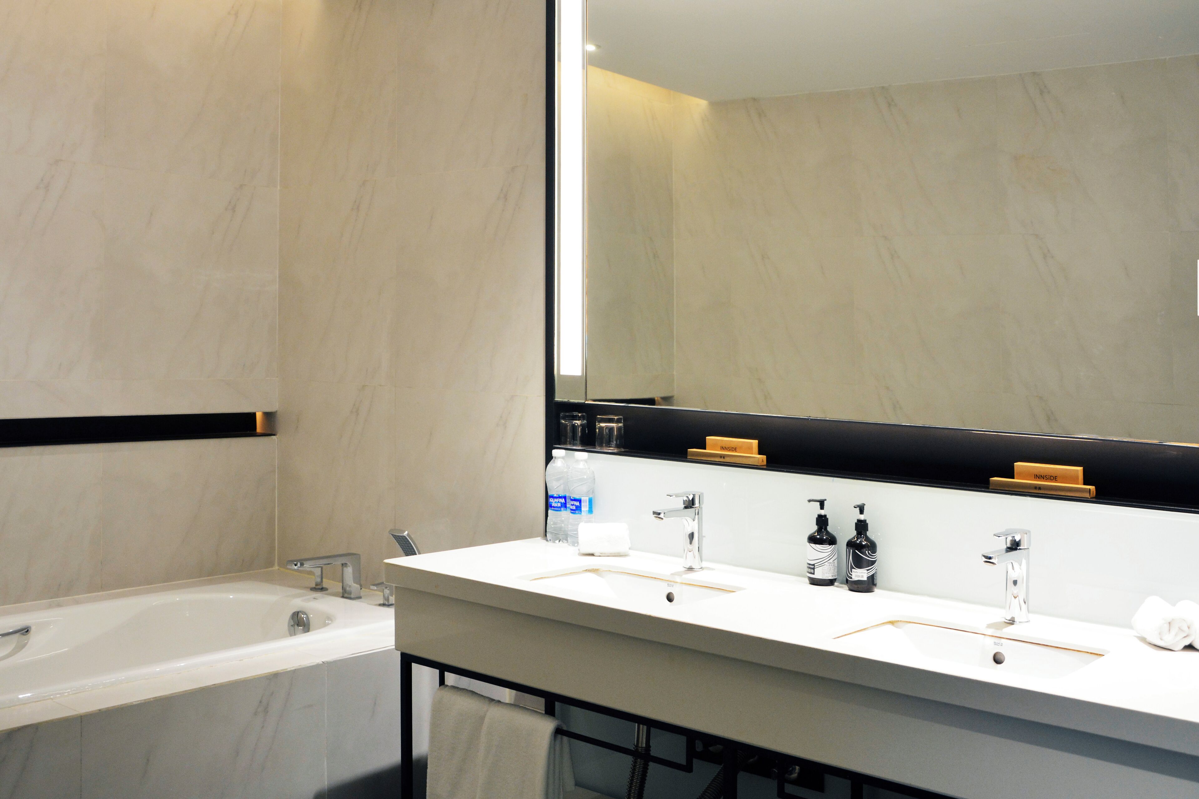 A modern bathroom with a large mirror, a bathtub, and a vanity with two sinks.