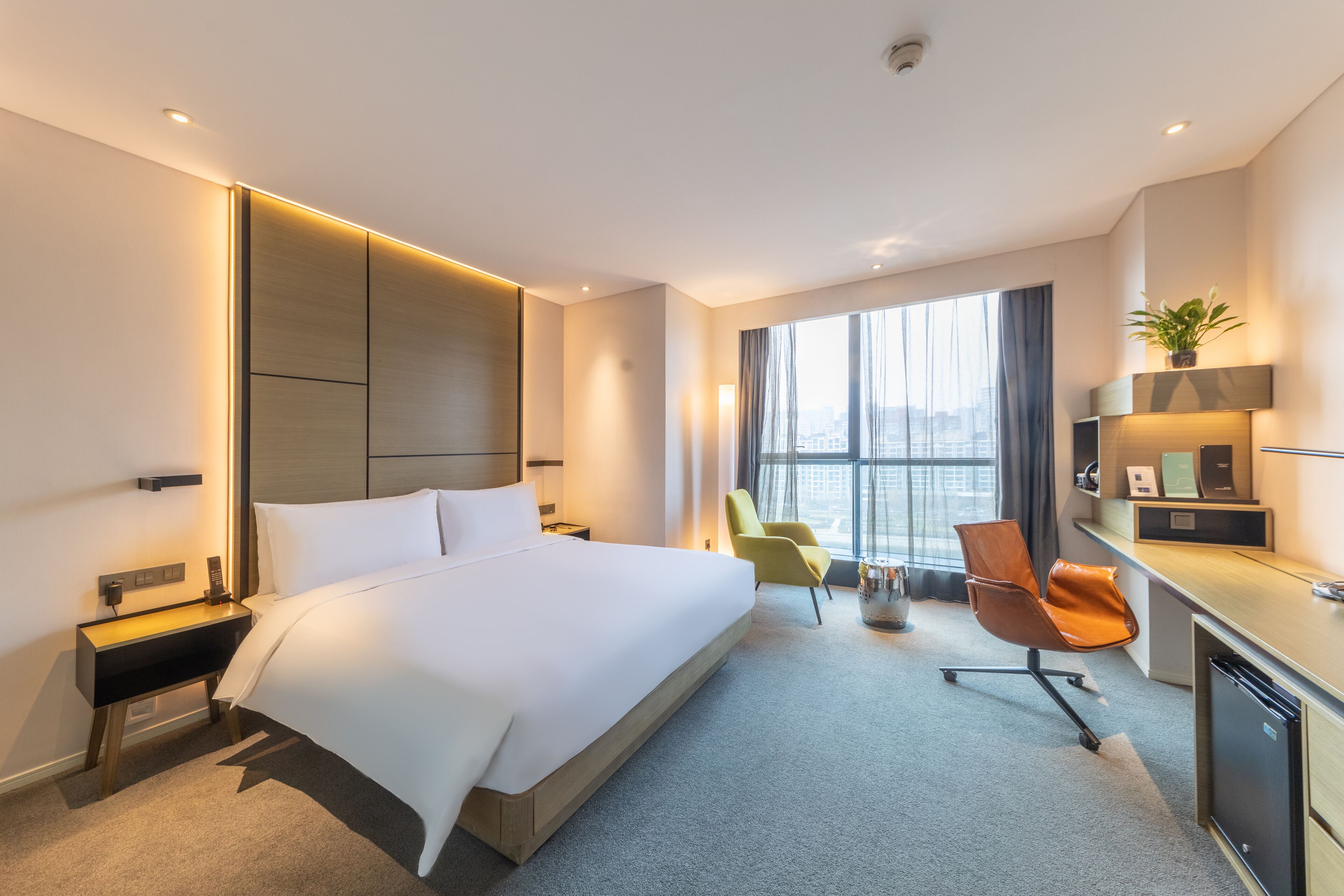 Een moderne hotelkamer met een groot bed, een bureau en een stoel. Er is een raam met uitzicht op de stad, en de kamer heeft een minimalistisch design.