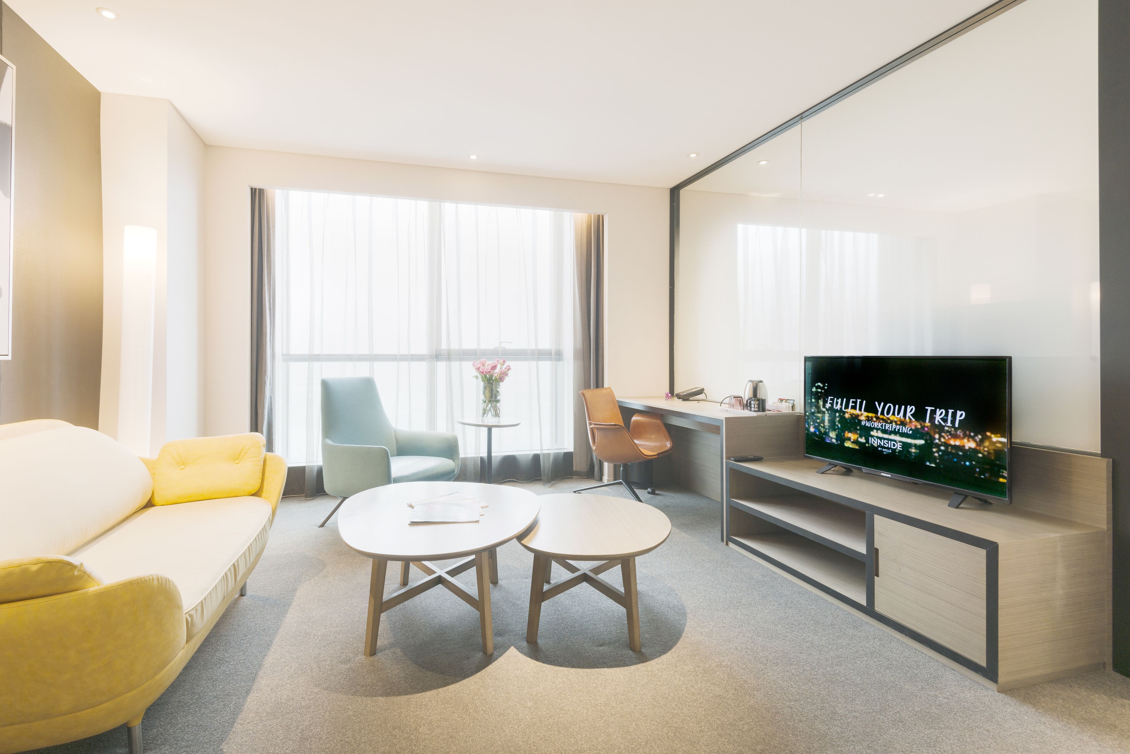 Une chambre d’hôtel moderne équipée d’un canapé, de deux petites tables rondes, d’une télévision et d’un bureau.