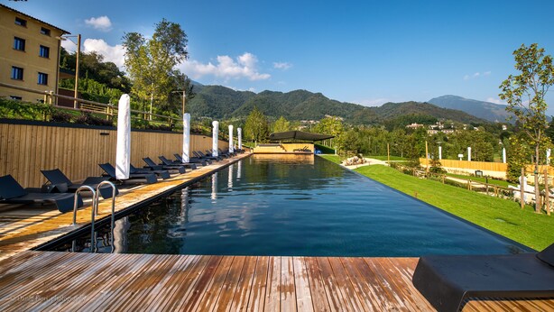 A swimming pool with a wooden deck, lounge chairs, and a view of mountains. - Podere La Torre (Schio)