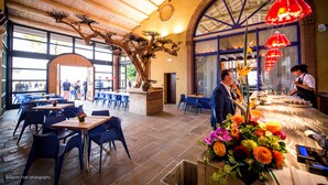 A restaurant interior with wooden ceiling beams, large windows, and a central dining area with tables and chairs. - Podere La Torre (Schio)