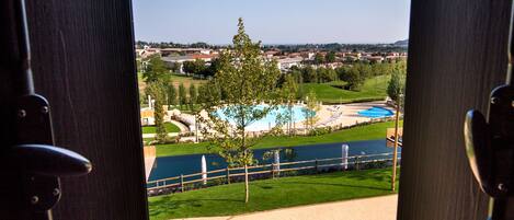 An open door revealing a view of a swimming pool, grassy areas, and distant buildings.