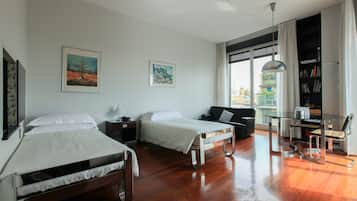 Ein Hotelzimmer mit zwei Betten, einem Schreibtisch mit Stuhl, einem Bücherregal und einem großen Fenster mit Vorhängen.