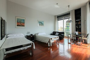 Habitación de hotel con dos camas, un escritorio con silla, una estantería y un ventanal con cortinas.