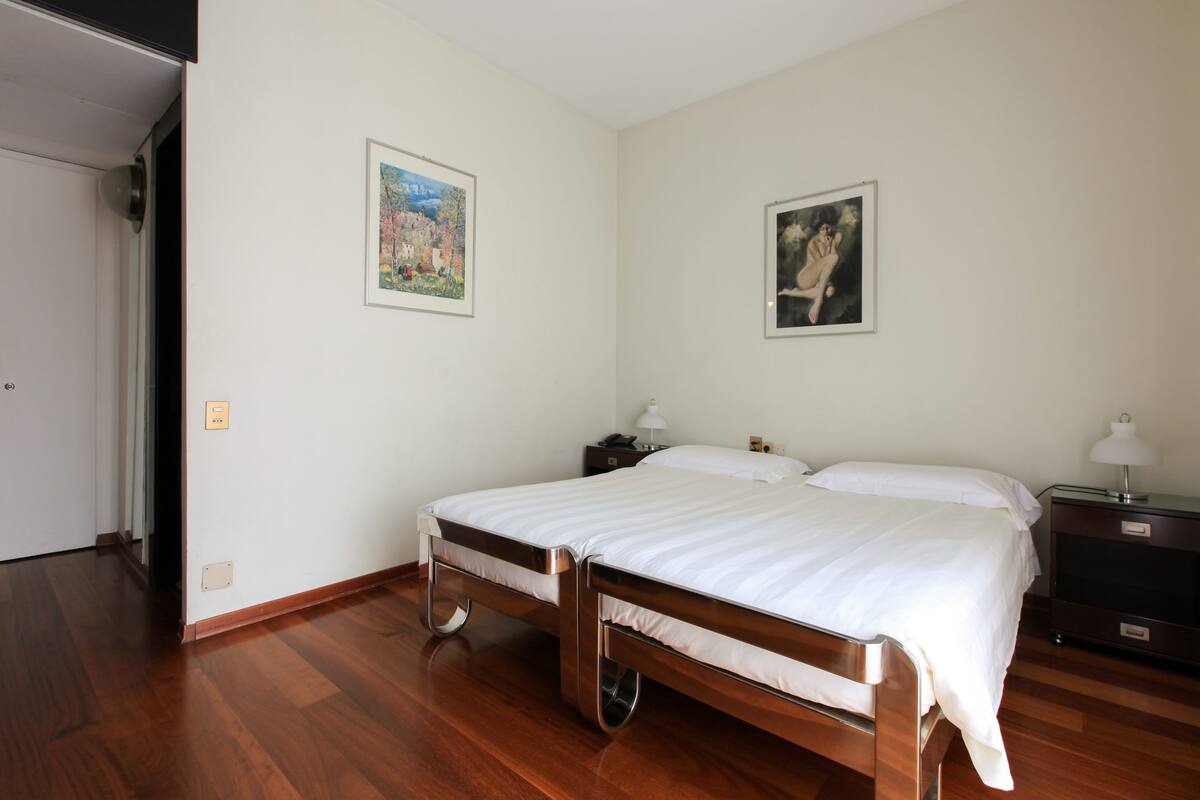 Un dormitorio con una cama de madera, dos mesitas de noche y dos cuadros enmarcados en las paredes.