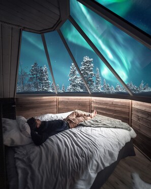 Et værelse med en seng, et vindue og udsigt til nordlys.