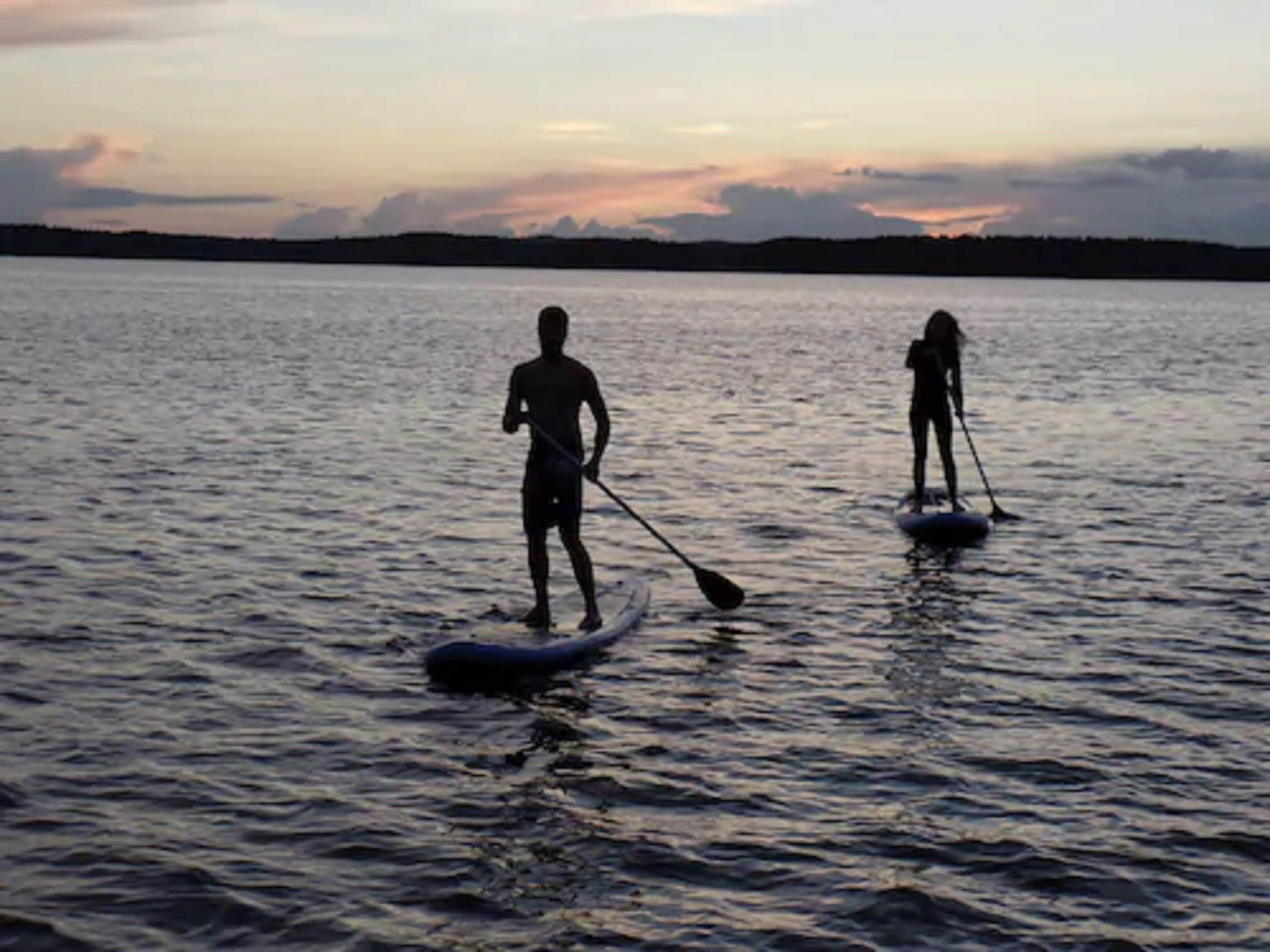 Dos personas hacen paddleboard en aguas tranquilas durante la puesta de sol.