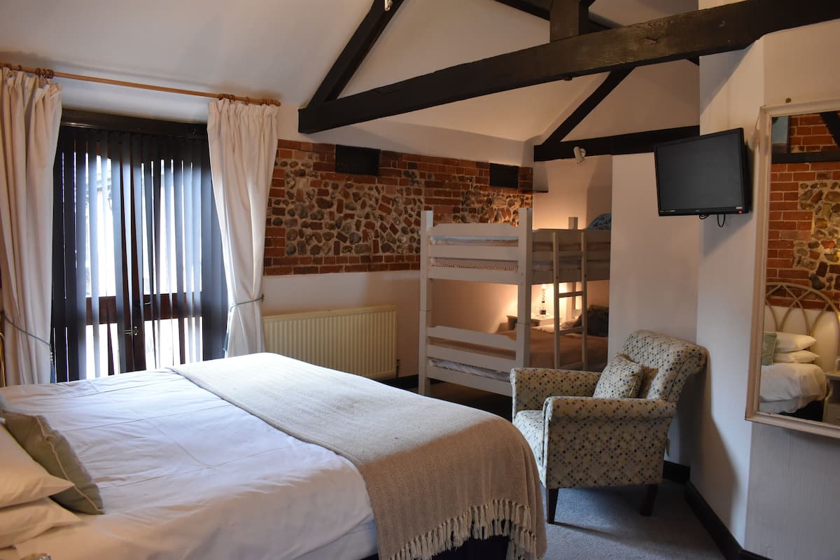 A bedroom with a bed, a chair, a TV, and a stone wall.