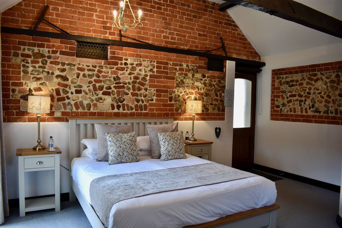 A bedroom with a brick wall, a bed with white bedding, two bedside tables with lamps, and a chandelier.