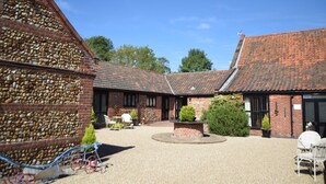 A courtyard with a gravel ground, a brick wall, and a building with a tiled roof. - At the Farmhouse Hunters Hall (Dereham)