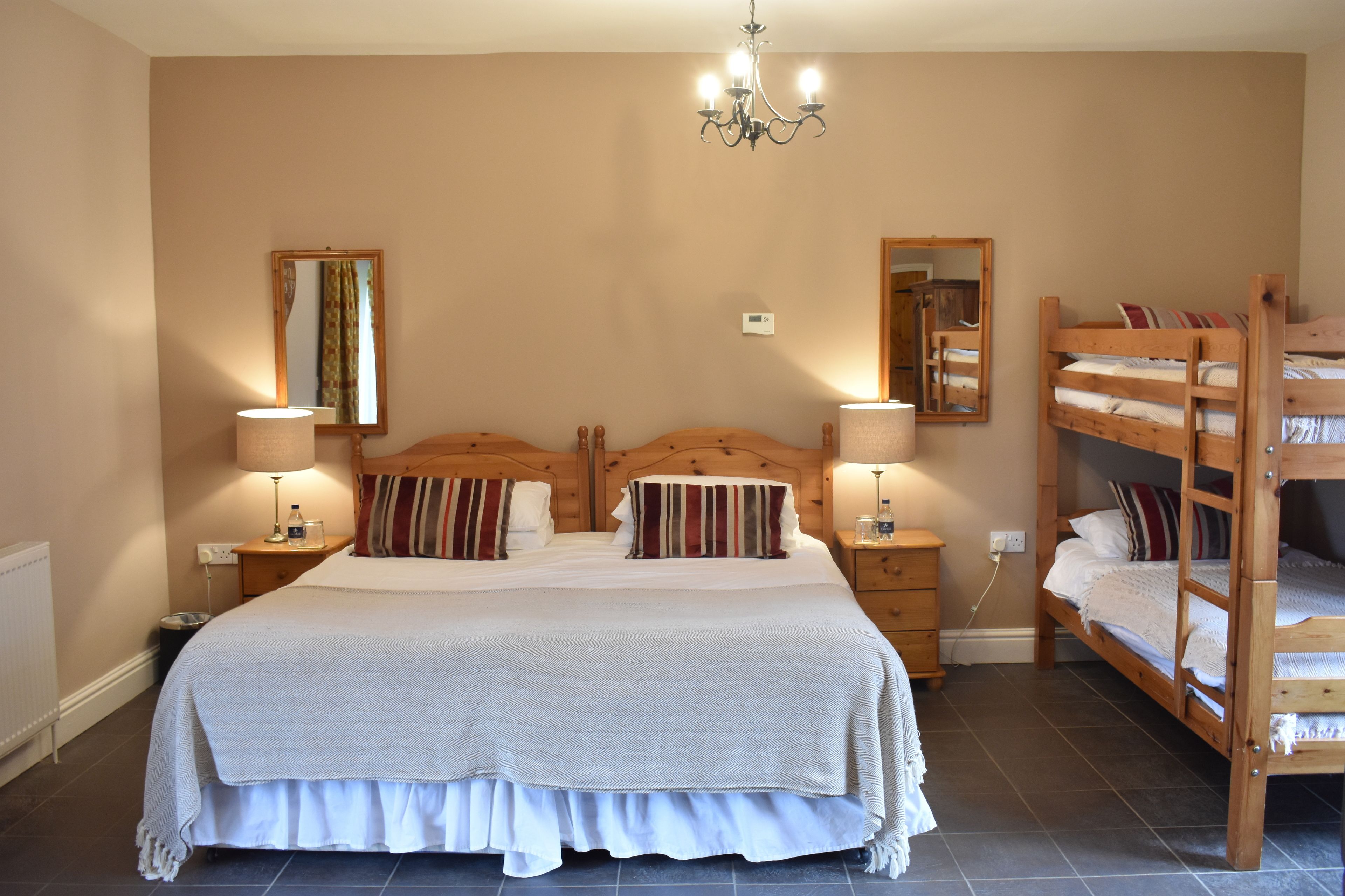 Ein Schlafzimmer mit einem großen Bett, zwei Nachttischen, einem Holzbettkasten und einer Deckenleuchte. An der Wand hängt ein Spiegel.