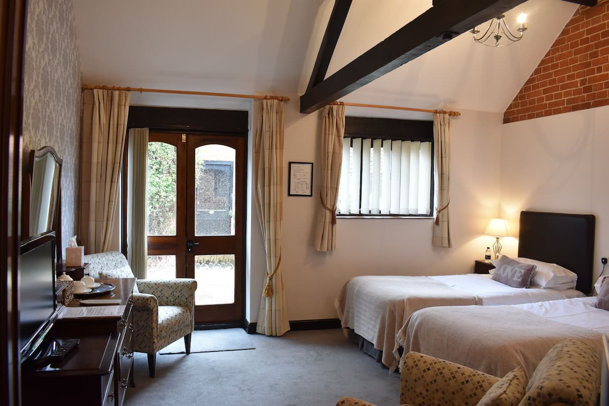 A hotel room with two beds, a desk with a chair, a window with curtains, and a chandelier.