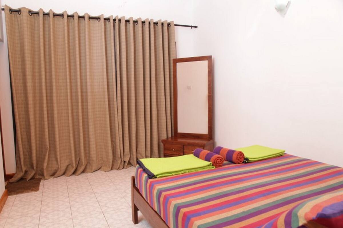 A bedroom with a bed, a wooden nightstand, a mirror, and beige curtains.