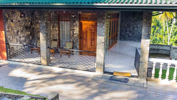 A house with a stone facade, a wooden door, and a covered porch with chairs. - AA Circuit bungalow (Kandy)