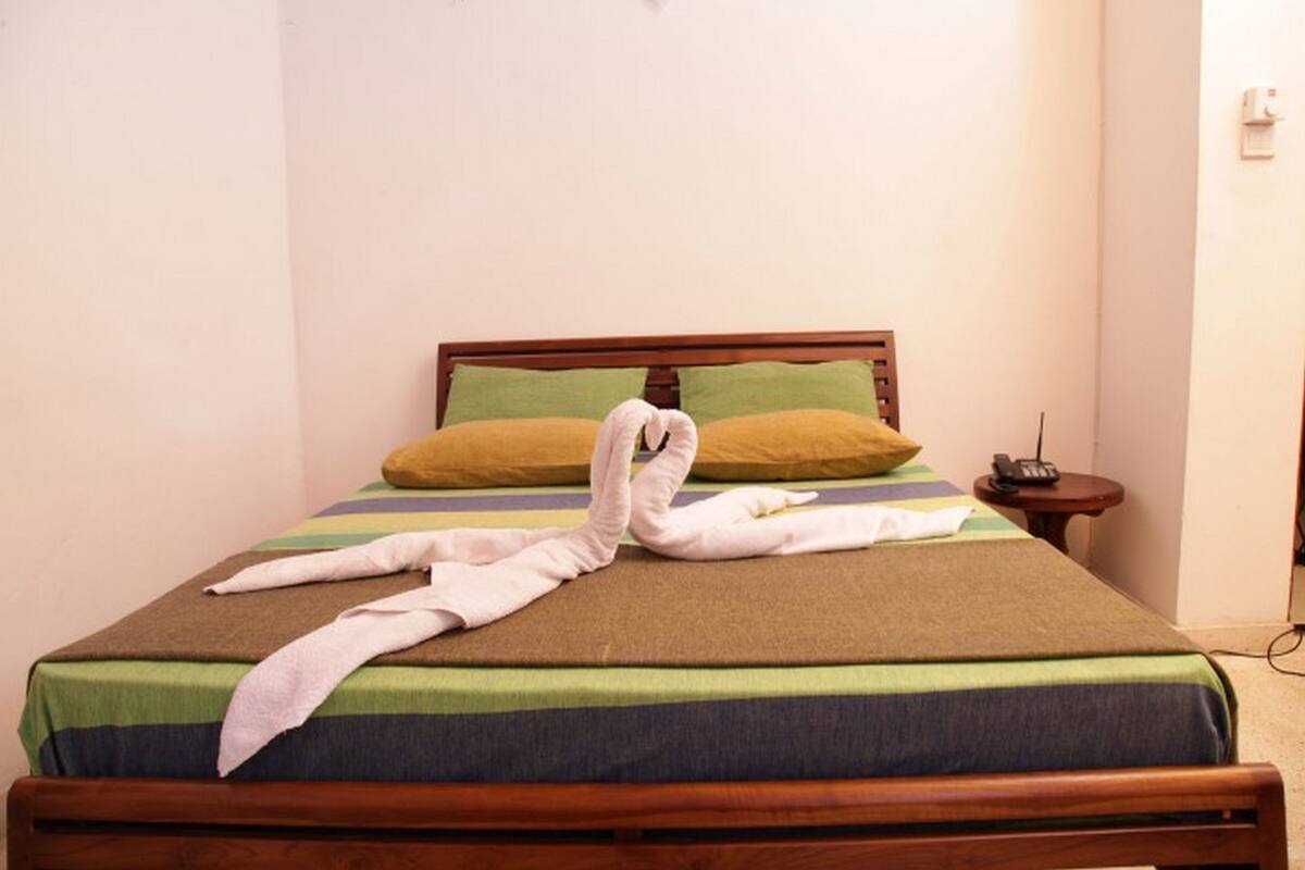 A neatly made bed with a striped bedspread, two pillows, and a towel arranged in a swan shape.