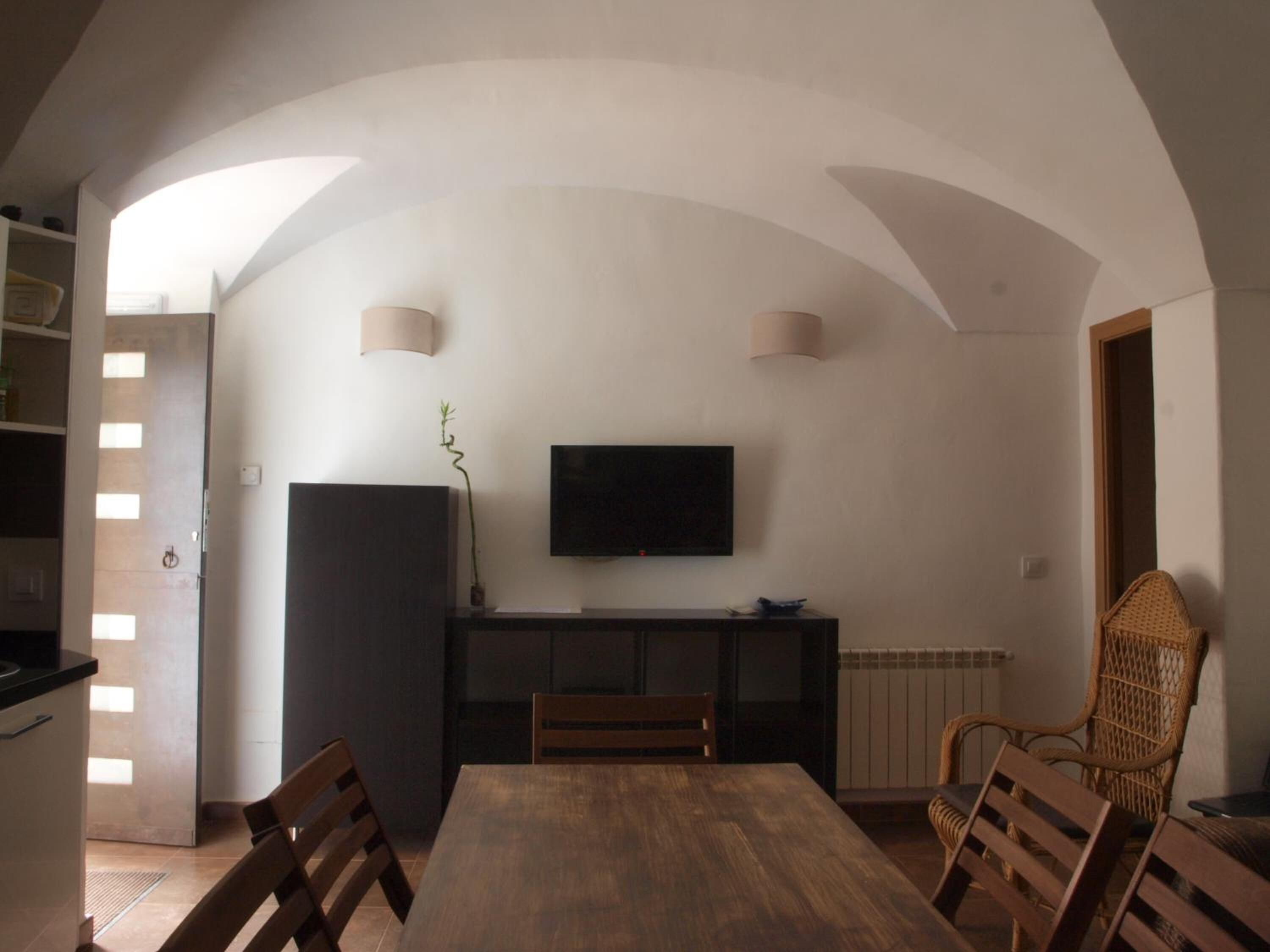 Un coin repas avec une table en bois, des chaises, un téléviseur fixé au mur et une plante posée sur la table.