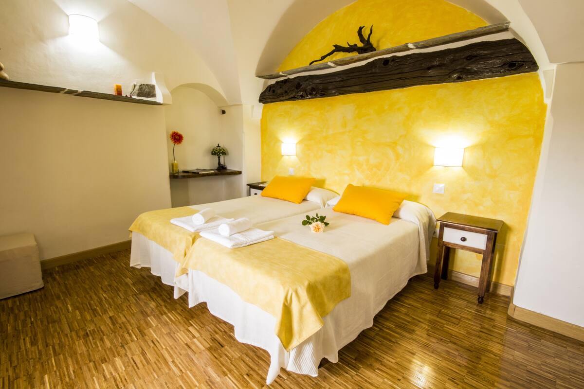 Une chambre d’hôtel avec deux lits, un plancher en bois, un mur d’accent jaune et une petite table de chevet.